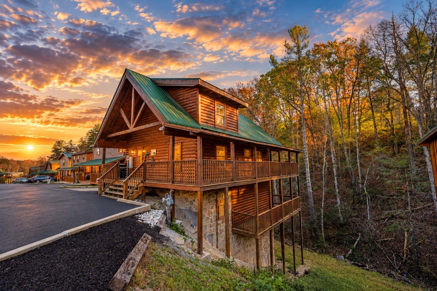 A wooden cabin with a balcony, surrounded by trees, and a parking area in front.