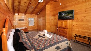 Un dormitorio de cabaña de madera con una cama, un televisor, un banco y una ventana.