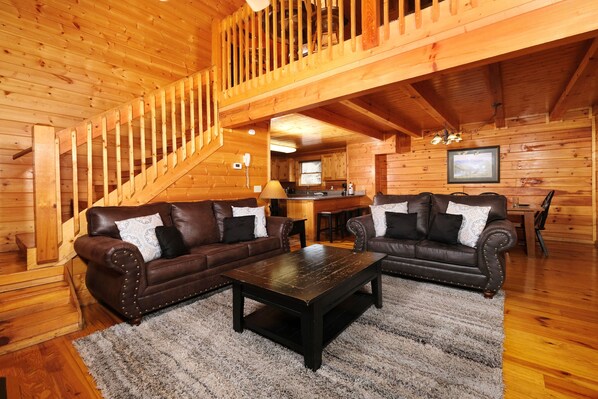 A wooden interior with two leather sofas, a coffee table, and a staircase.