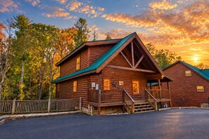 A log cabin with a green roof, a porch, and a staircase leading to the entrance. - Creekside Delight: Your Delightful Mountain Escape (Pigeon Forge)