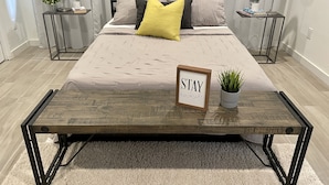 Ein modernes Schlafzimmer mit Bett, Nachttischen, Lampen, einem kleinen Topfpflanzen und einem motivierenden Spruch auf dem Bett.