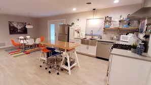 Eine moderne Küche mit weißen Schränken, einem Edelstahl-Kühlschrank, einer Mikrowelle und einem Spülbecken. Ein Essbereich mit Tisch und Stühlen lädt zum Verweilen ein, und ein farbenfroher Teppich liegt auf dem Boden.
