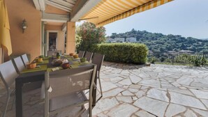 Un patio exterior con suelo de piedra, una mesa preparada para comer y vistas a una colina.