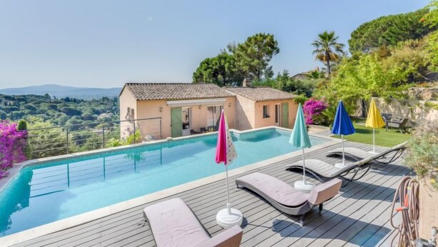 Piscina con sillas de descanso y sombrillas, rodeada de una casa y vegetación exuberante.