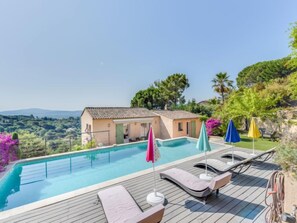 Ein Schwimmbecken mit Liegestühlen und Sonnenschirmen, umgeben von einem Haus und üppiger Bepflanzung.