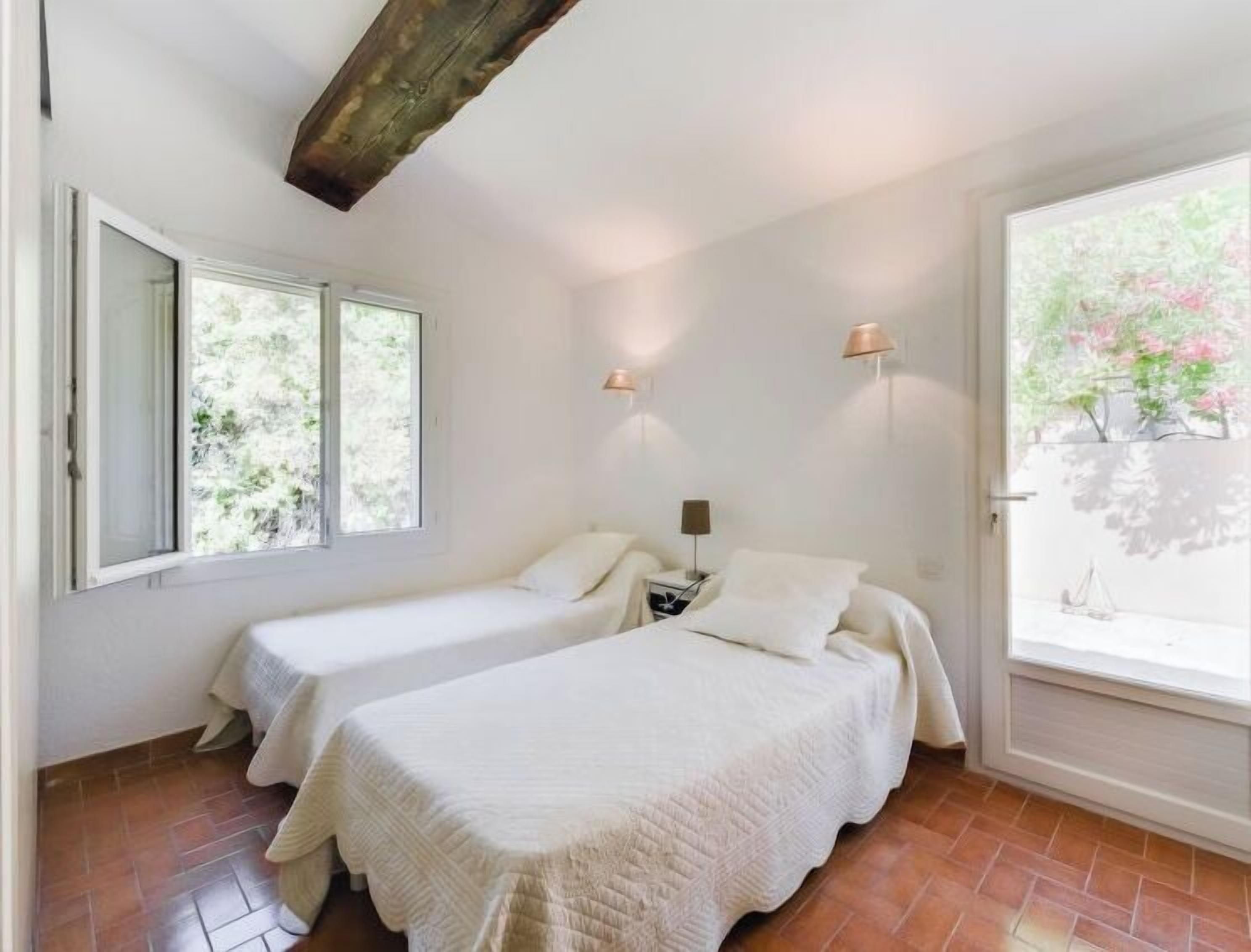 A bedroom with two beds, a window, and a view of trees.