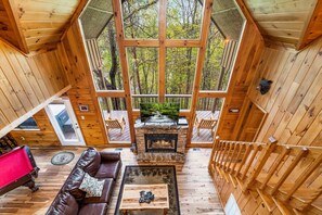 Eine Holzhütte mit Kamin aus Stein, einer Holzterrasse und einem großen Fenster mit Blick auf einen Wald.