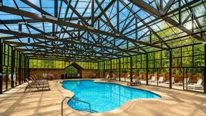 An indoor swimming pool with a glass ceiling, lounge chairs, and a stone wall. - Raccoons' Rest: Kick Back in the Smokies (Pigeon Forge)