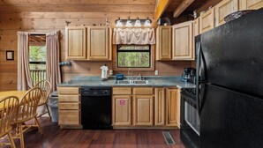 Cocina de cabaña de madera con un refrigerador negro, armarios de madera, un lavabo y un comedor con sillas.