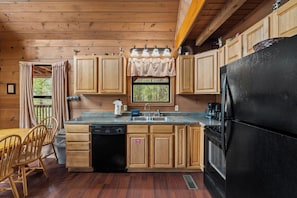 A wooden cabin kitchen with a black refrigerator, wooden cabinets, a sink, and a dining area with chairs.