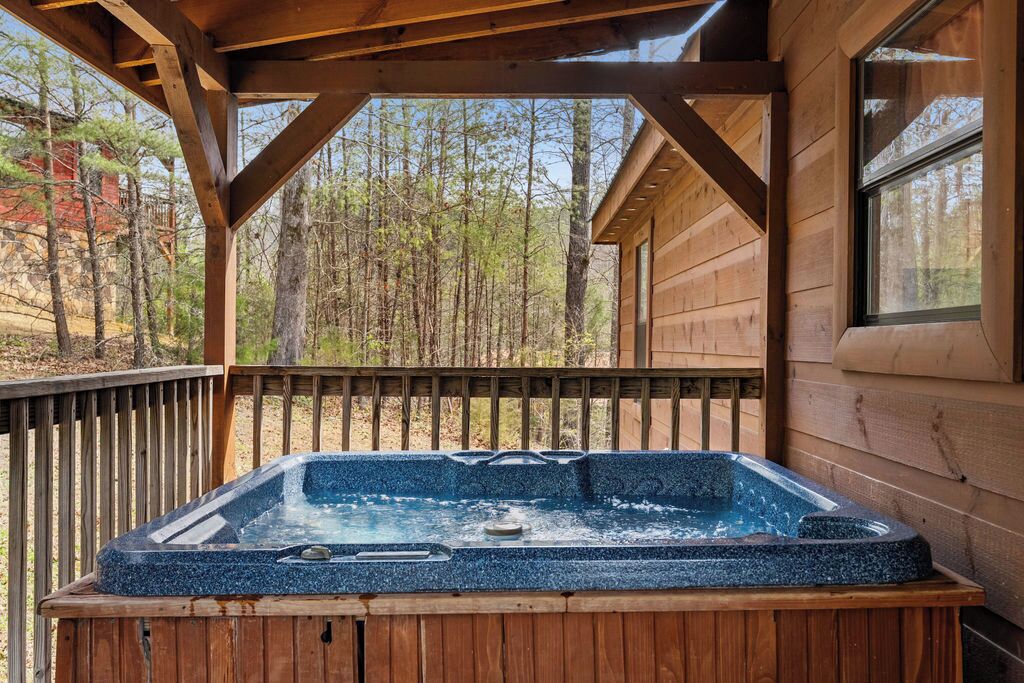 Een houten terras met een jacuzzi, omgeven door bomen en een houten hut.