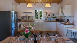 A modern kitchen with wooden beams, a stainless steel refrigerator, white cabinets, and a dining area set for six with a table, chairs, and a vase of flowers. - Villa Klara in Klarići (Klarići)
