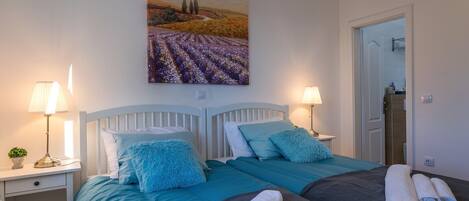 Ein Hotelzimmer mit zwei Betten, einem Bild von einem Feld und einem durchgegangenen Tür sichtbar erkennbaren Badezimmer.