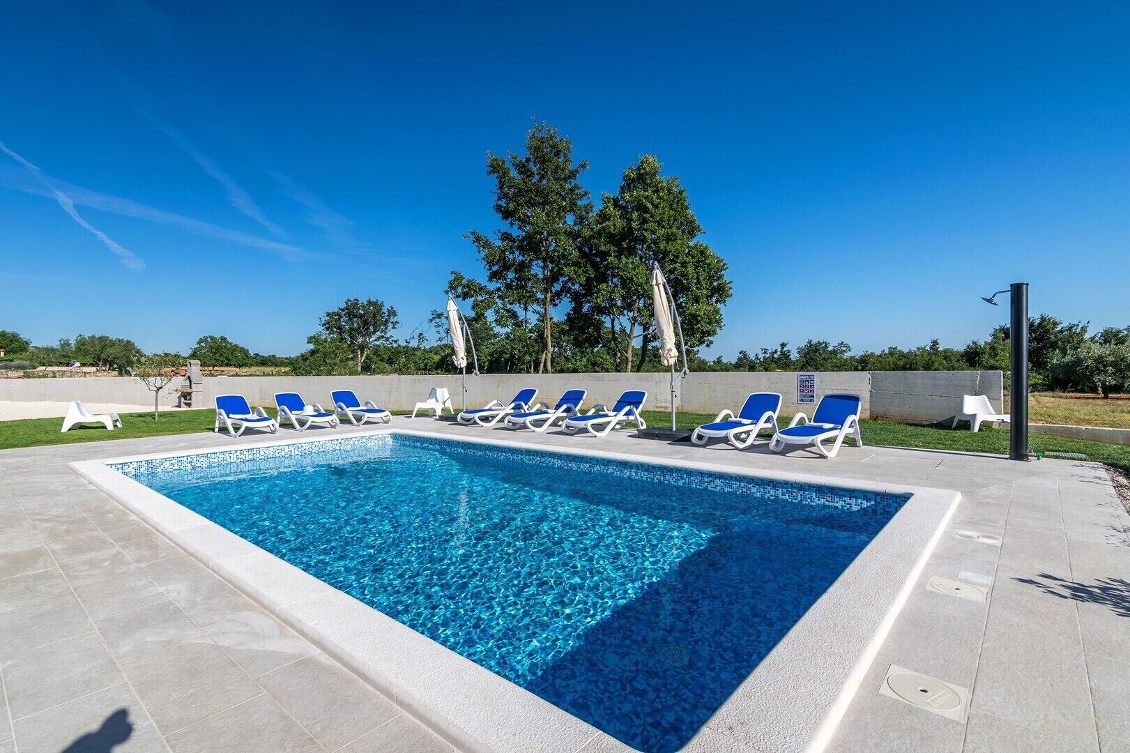 Une piscine rectangulaire à l’eau d’un bleu limpide, entourée d’une terrasse carrelée. Plusieurs chaises longues bleues sont alignées le long du bord de la piscine.