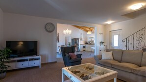 A modern living room with a flat-screen TV, a glass coffee table, a sofa, and a dining area visible through an open doorway. - Villa Klara in Klarići (Klarići)