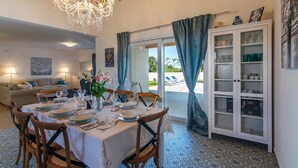 A dining area with a chandelier, dining table set for six, and a view of a pool through a glass door. - Villa Klara in Klarići (Klarići)