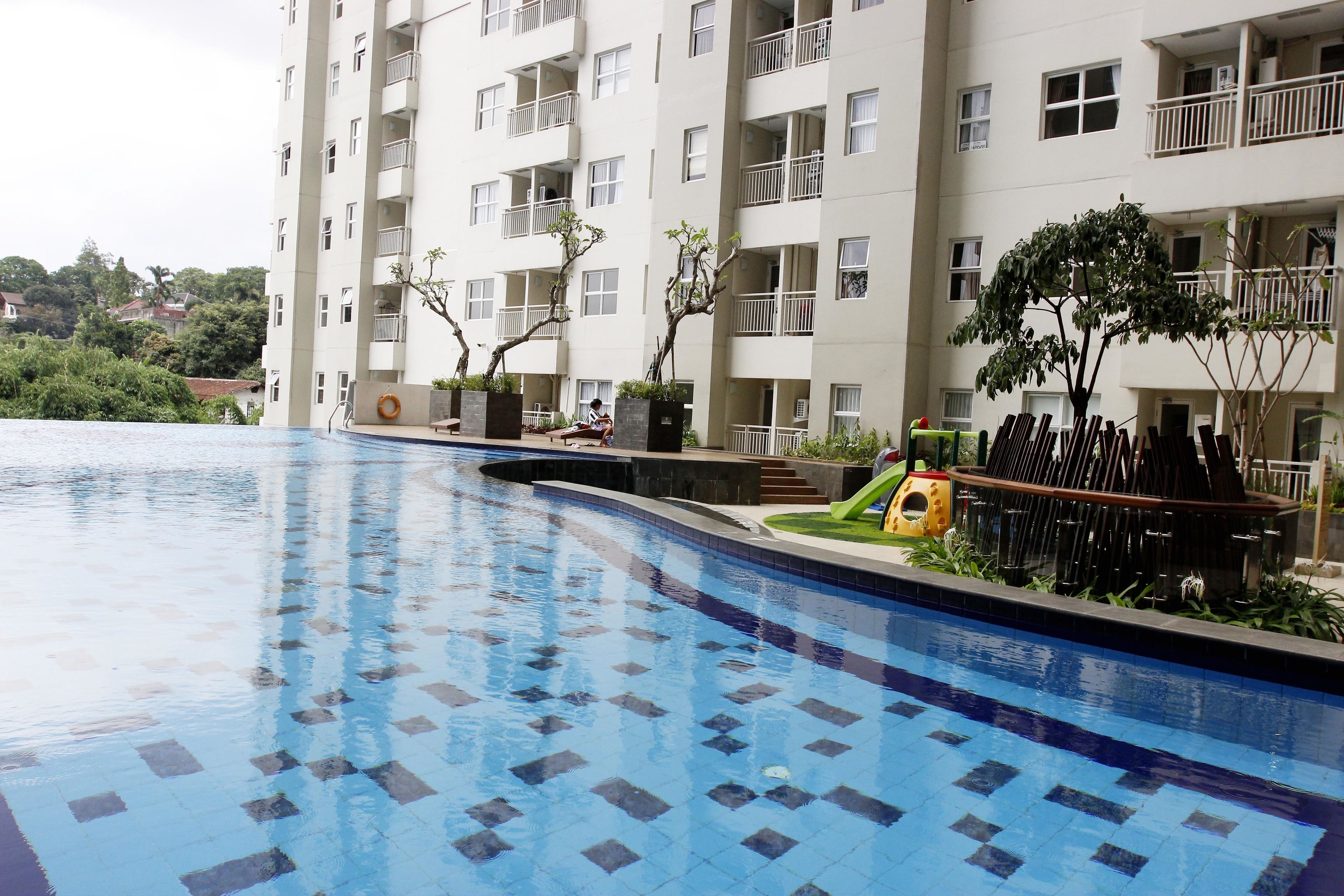 Una piscina con suelo de baldosas, rodeada por un edificio de varios pisos con balcones y plantas en macetas.