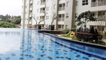 Una piscina con suelo de baldosas, rodeada por un edificio de varios pisos con balcones y plantas en macetas.