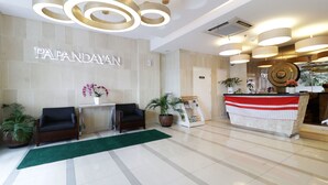 A modern reception area with a sign reading "PAPANDAYAN," a reception desk, two sofas, and potted plants. - Ten Eleven Living Point (Bandung)