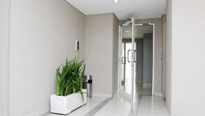 A modern hallway with a potted plant, a trash bin, and a glass door leading to another room. - Ten Eleven Living Point (Bandung)