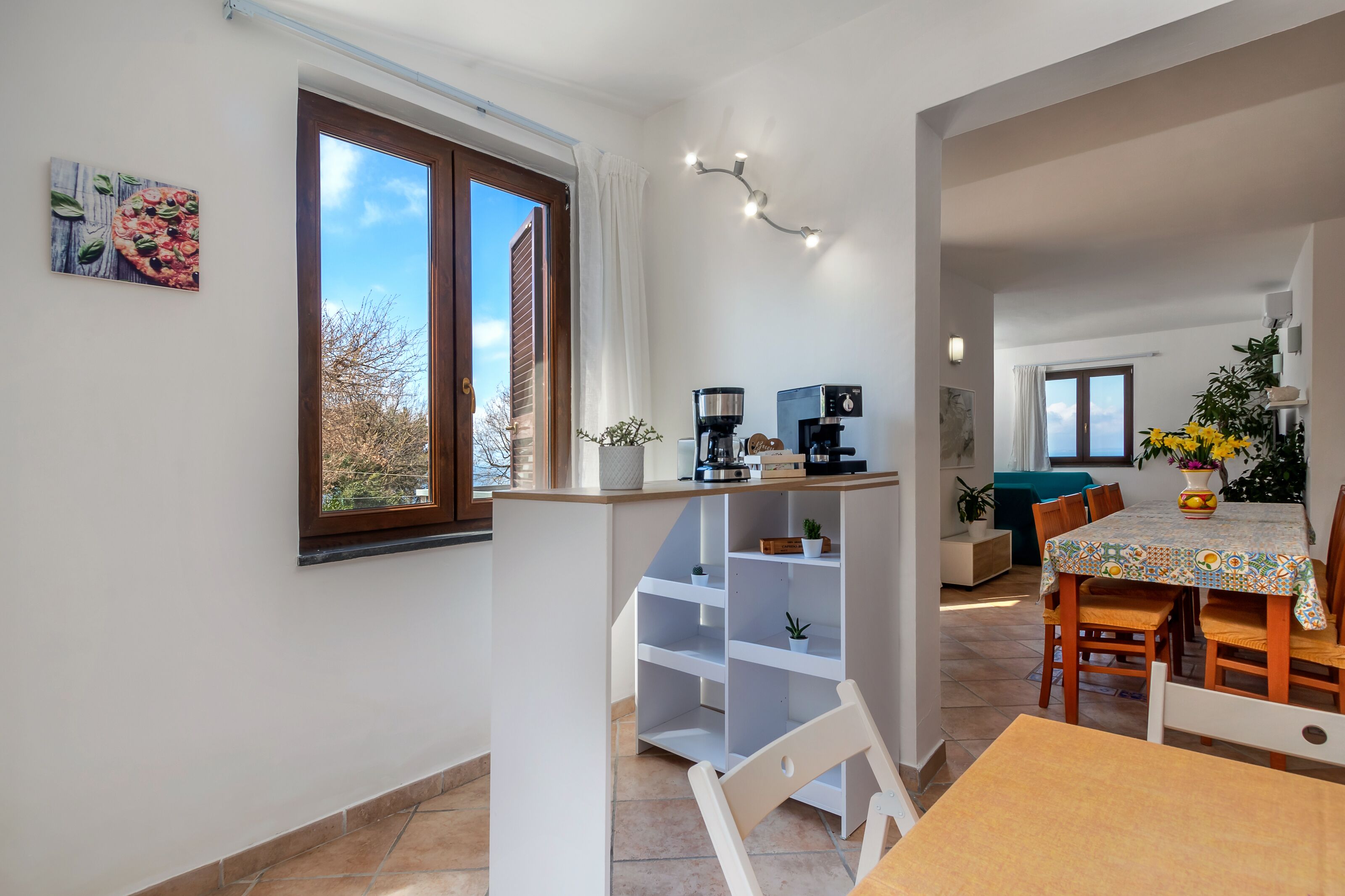 Una cocina moderna con comedor, que incluye una cafetera, una planta pequeña y vistas al exterior.
