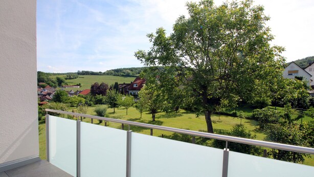 Un balcone con ringhiera in metallo che si affaccia su un paesaggio rurale con case e alberi.
