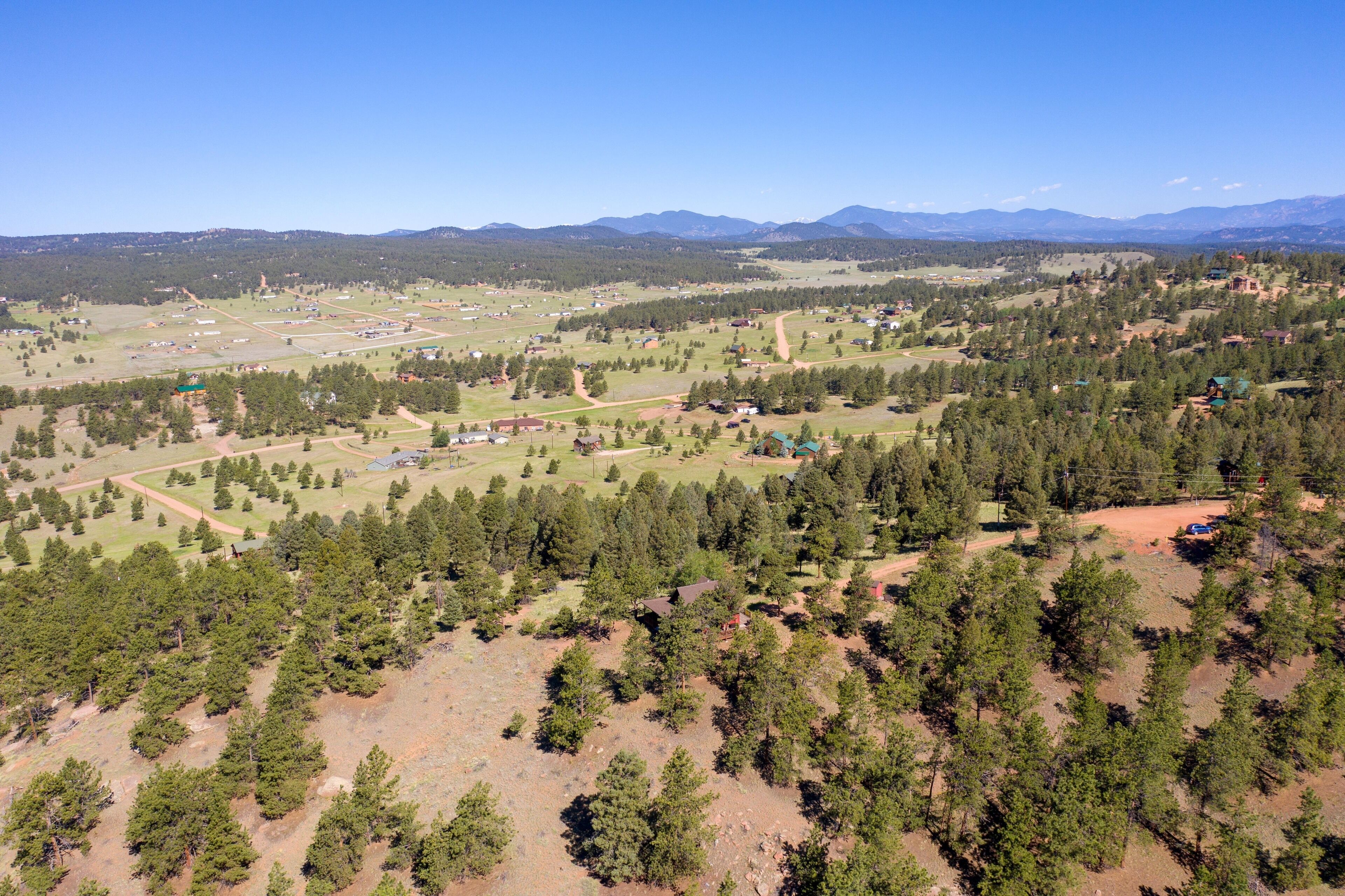 An aerial view of a rural area with scattered houses, dense forests, and mountains in the background.