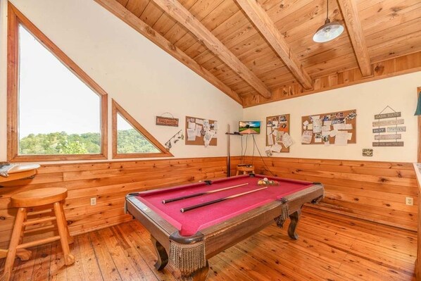 Una sala con paneles de madera, una mesa de billar, taburetes de madera y un televisor.