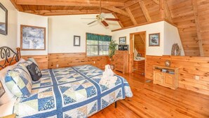 Un dormitorio acogedor con techo de madera, cama con colcha, cómoda y ventana con cortinas.