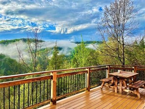 A wooden deck with a table and benches, overlooking a forested valley with mist and a clear sky. - A Mountain Haven: Your Quiet Mountain Escape (Sevierville)
