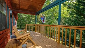 Eine Holzterrasse mit Liegestühlen und einem überdachten Bereich, umgeben von Bäumen.