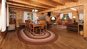Interior de una cabaña de madera con comedor, sofás y chimenea.