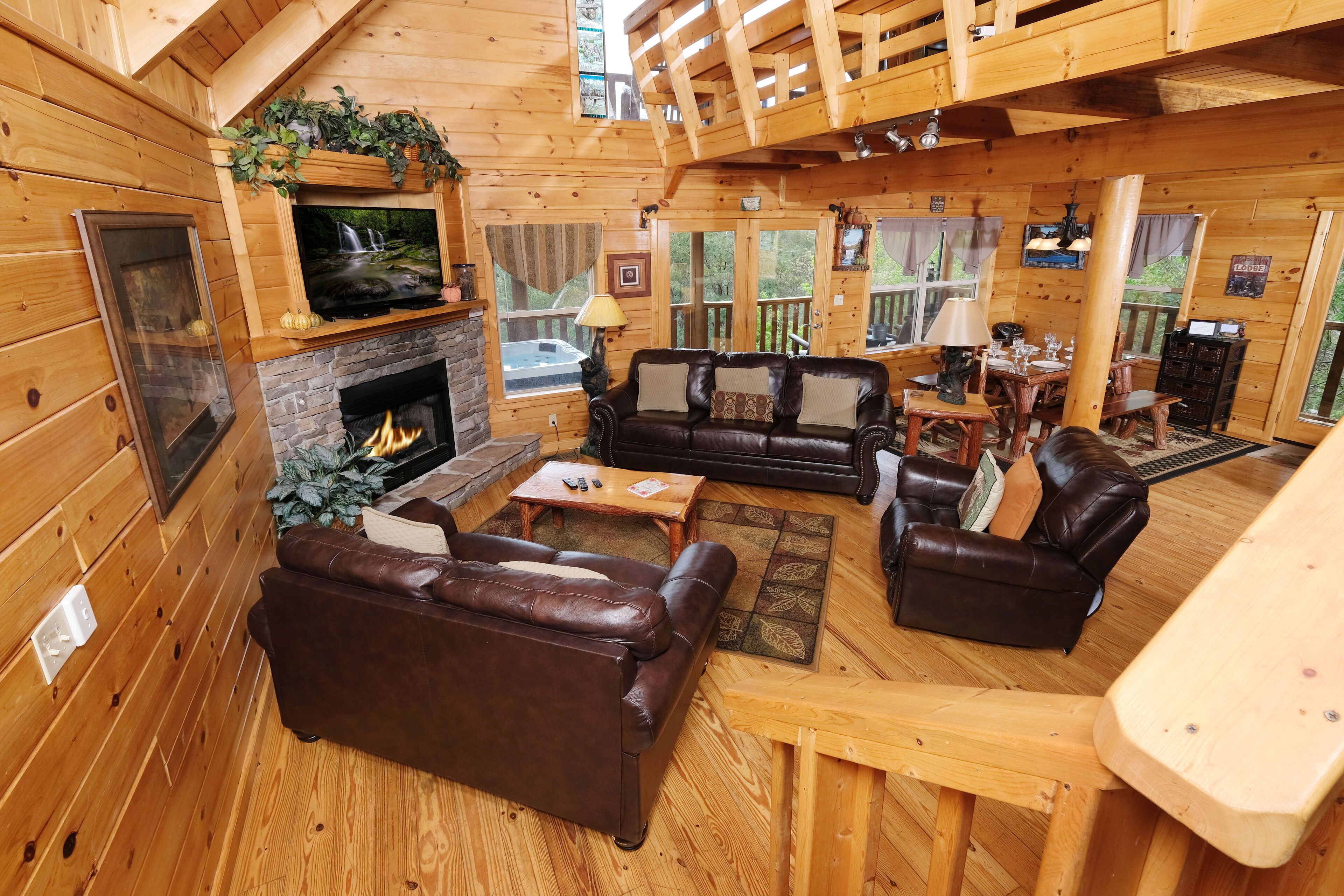 Interior acogedor de una cabaña con chimenea, sofás de cuero, suelo de madera y un televisor sobre la chimenea.
