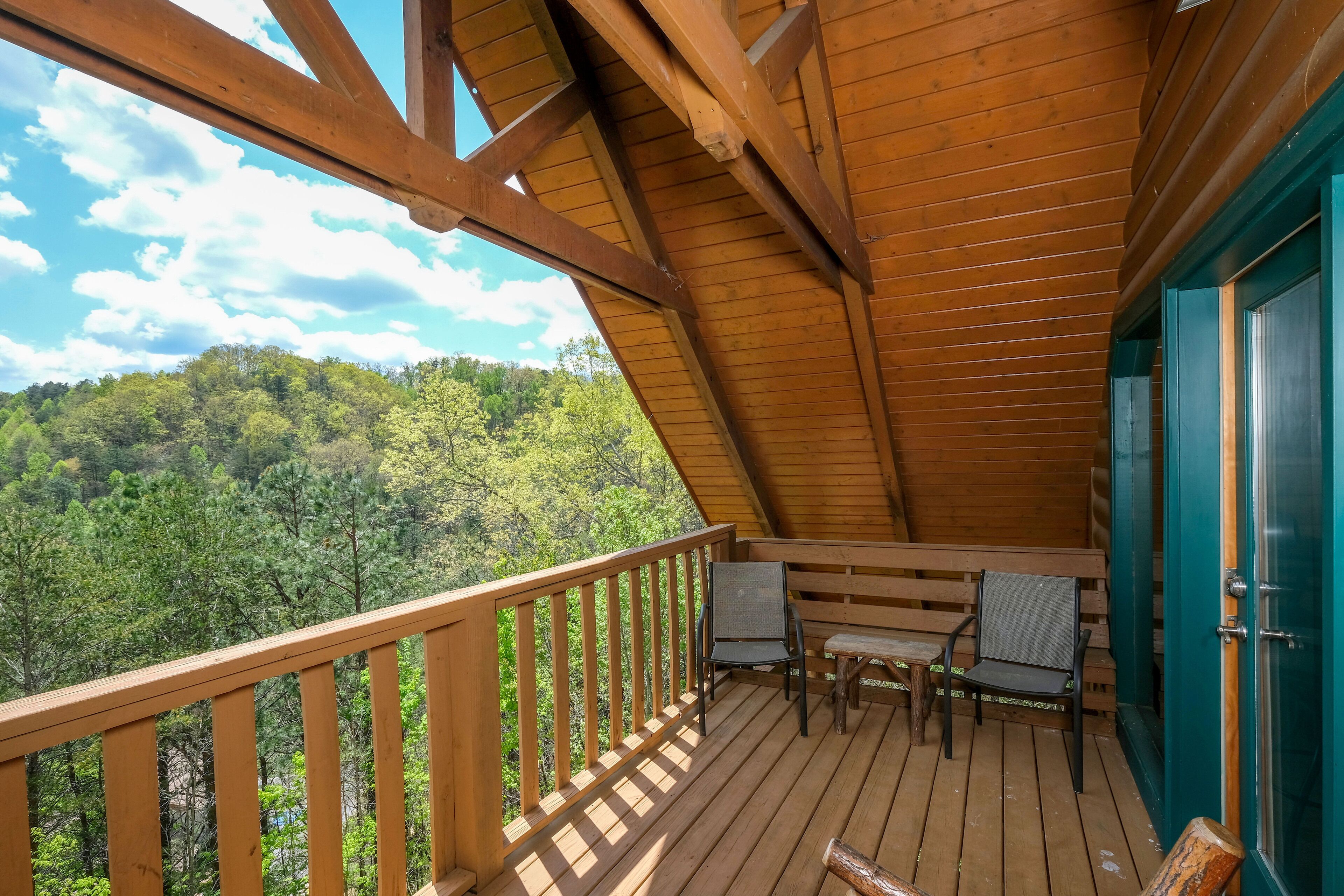 A wooden deck with a view of a forested hill, a table with chairs, and a door.