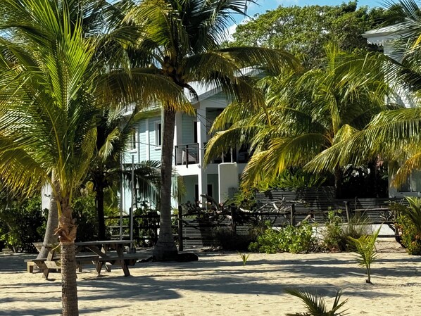 Una propiedad frente a la playa con un edificio de dos pisos, palmeras y una zona de arena.
