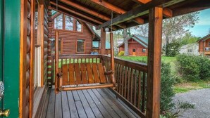 A wooden deck with a swing chair, a green door, and a view of cabins in the background. - Bear Ridge: Stay on the Wild Side (Pigeon Forge)