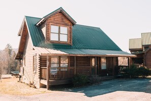 A rustic log cabin with a green metal roof, a porch with a sign, and a gravel driveway. - Bear Ridge: Stay on the Wild Side (Pigeon Forge)