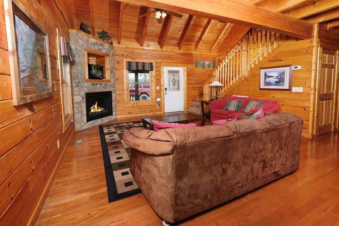 Ein Blockhaus-Interieur mit Kamin, Holzwänden, einer Couch und einer Treppe.