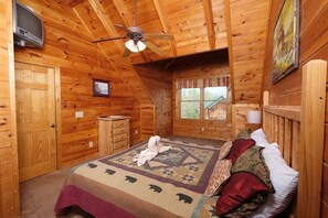 A wooden cabin bedroom with a bed, a ceiling fan, a television, and a window with curtains. - Bear Ridge: Stay on the Wild Side (Pigeon Forge)