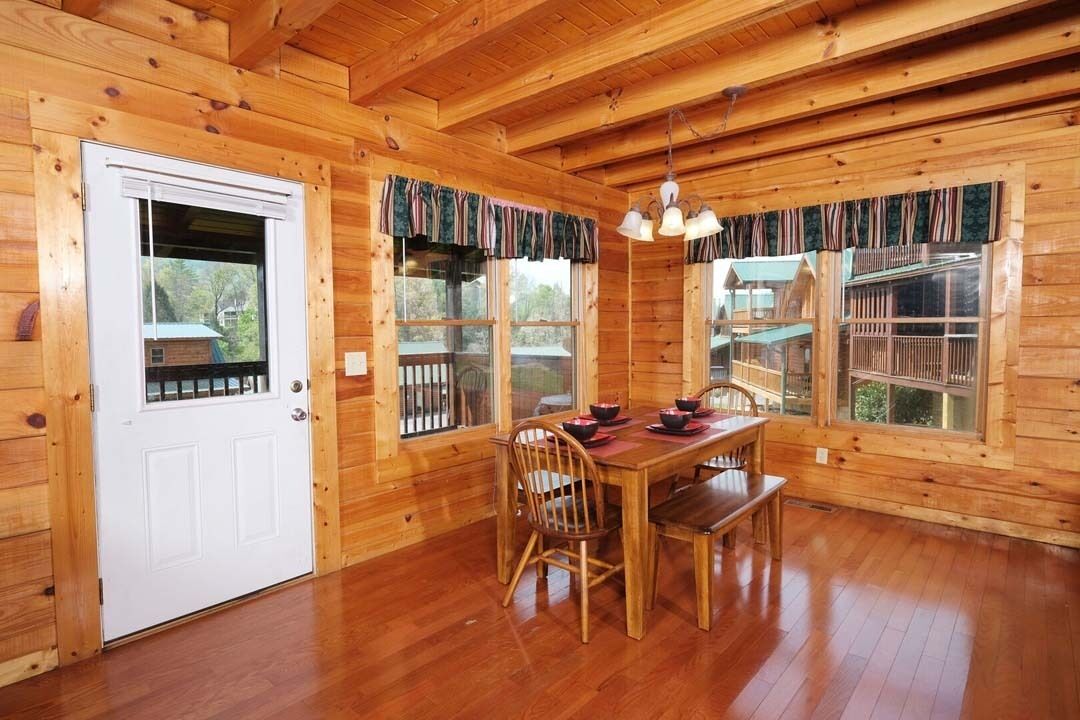 L’intérieur d’un chalet en bois, avec une table et des chaises, une porte blanche et des fenêtres avec des rideaux.