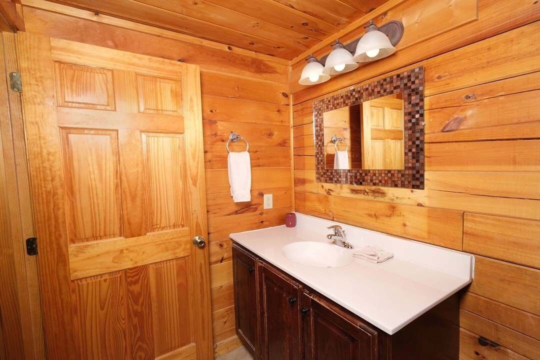 A wooden cabin-style bathroom with a wooden door, a white sink, and a mirror with a mosaic frame.