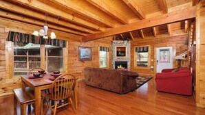 A wooden cabin interior with a dining area, a fireplace, and a red sofa. - Bear Ridge: Stay on the Wild Side (Pigeon Forge)