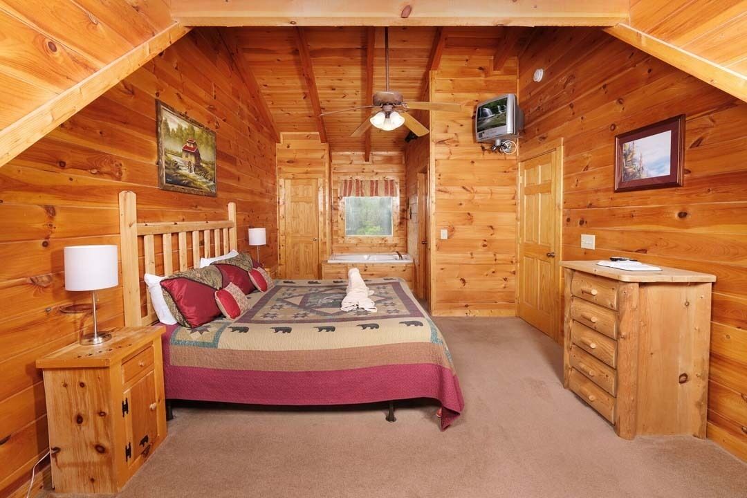 A cozy wooden cabin bedroom with a bed, dresser, and a ceiling fan.