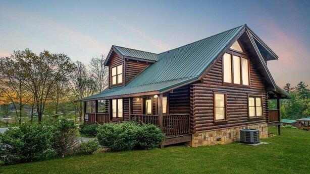 A log cabin with a stone foundation, a green metal roof, and a porch with railings. - Bear Ridge: Stay on the Wild Side (Pigeon Forge)