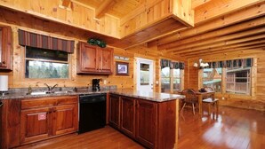 A wooden cabin interior with a kitchen featuring wooden cabinets, a sink, and a dining area with a table and chairs. - Bear Ridge: Stay on the Wild Side (Pigeon Forge)