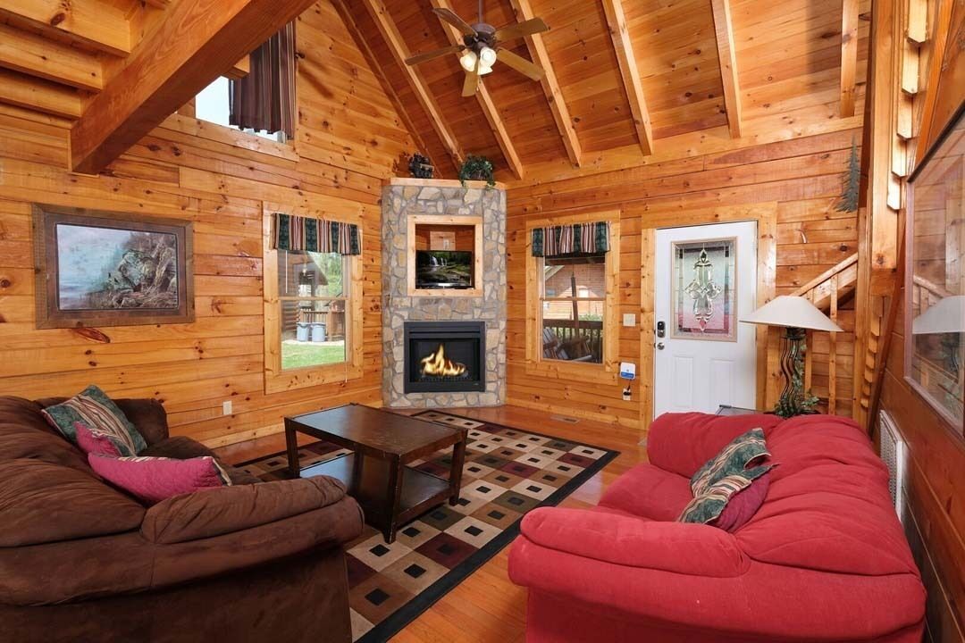 A log cabin interior with a fireplace, wooden walls, and a cozy seating area.