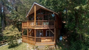 Eine zweistöckige Holzhütte mit Balkon, umgeben von dichtem Wald.