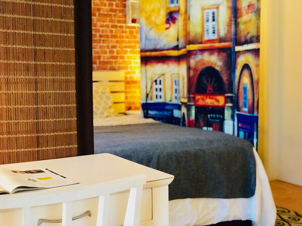 A room with a bed, a white bedside table with drawers, and a colorful mural on the wall.