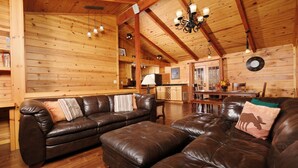 A cozy wooden interior with a leather sofa and ottoman, wooden beams, and a chandelier.