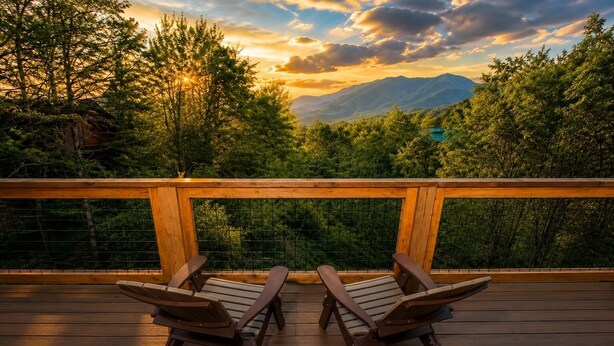 A wooden deck with two rocking chairs facing a mountainous landscape.
